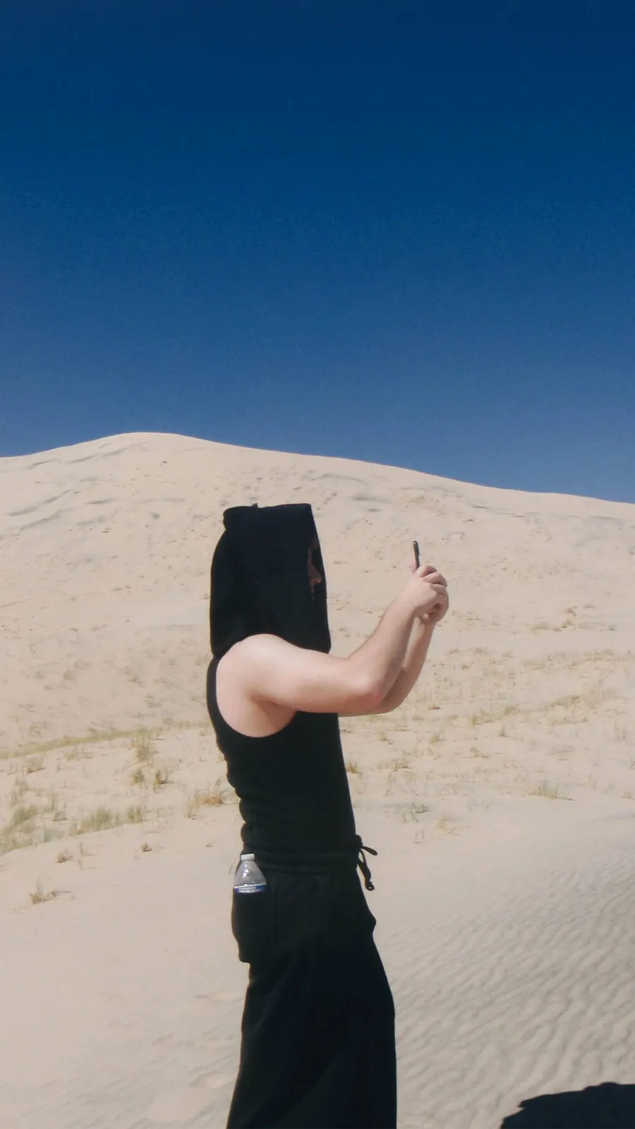 Rafa Villaseñor in a black hooded tank at the top of a sand dune, taking a photograph.